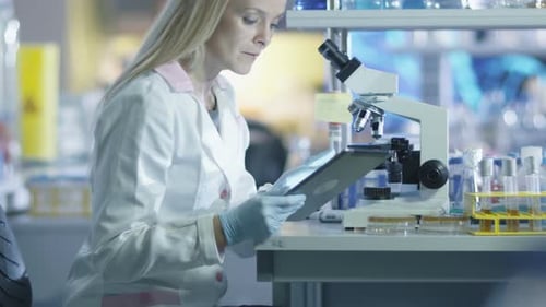 Female Scientist Using Microscope and Tablet in Lab