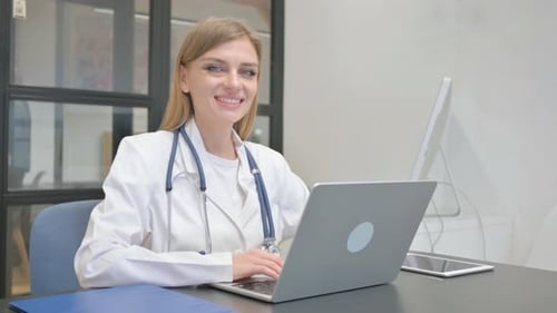 Female Doctor Working on Laptop, Smiling at Camera
