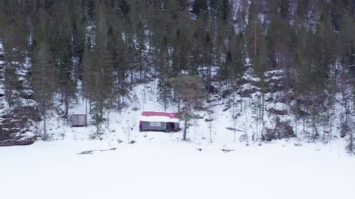 Winter Season On The Countryside With Cottage And Dense Forest. Aerial Lateral Shot