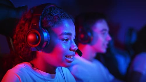 White boy and black girl teens in headsets playing video games in video game club with blue and red