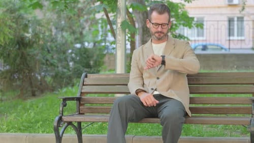 Man Waiting on Park Bench Looking at Watch