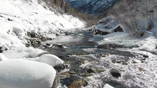 Low aerial flight up babbling, snowy white, frozen stream in winter
