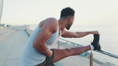 Young athlete doing warm-up, stretching legs before training while standing on the embankment