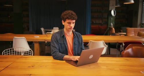 Focused Male Student Working on Laptop in University Library or in Modern Coworking