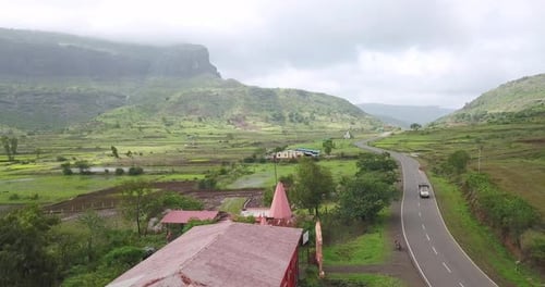Veículos dirigindo na estrada de asfalto entre campos em Trimbakeshwar, Índia, sob nuvens de monção - um