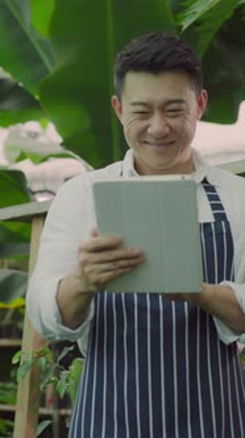 Asian Professional Young Farmer Holding Computer Tablet Browsing Data and Controling Cultivation