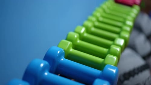 Closeup Blue and Green Vinyl Dumbbells Lying on a Sports Equipment Rack in the Gym