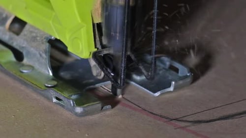 Close-up of electric jigsaw in action, men's hand cutting up wood board with a jigsaw in slow motion