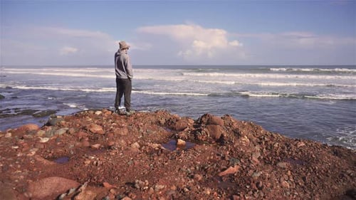 Homem caminha na praia rochosa e olha para as ondas do mar nas férias de verão