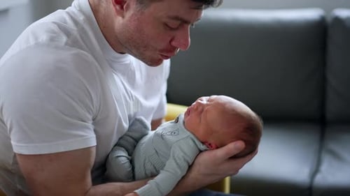 Little newborn boy is crying in dad’s hands. Father tries to sooth his child waving him.