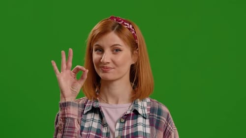 Junge fröhliche kaukasische Frau zeigt OK-Zeichen auf Greenscreen-Hintergrund Chroma Key