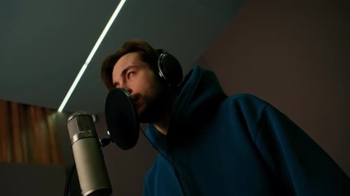 Rap singer with headphones and microphone emotionally recording new song in professional studio