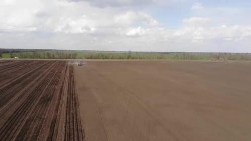 Blue tractror planting sunflower with yellow planter on the cultivated field in Ukraine