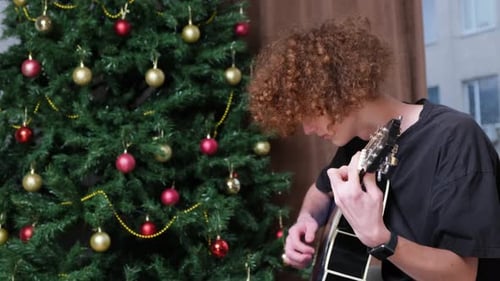 Young Adult Playing Guitar by Christmas Tree