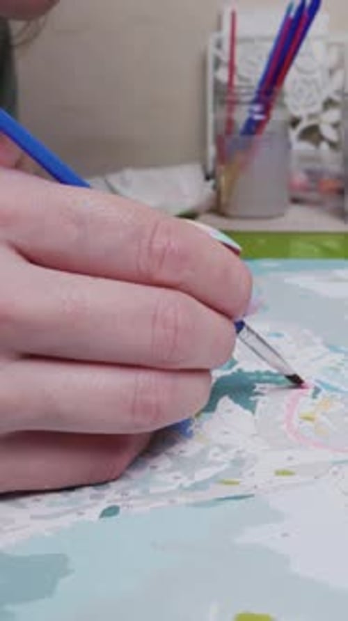 The young woman paints a picture by numbers with paints with a brush, in motion, close-up. Vertical