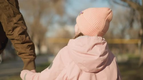 Little Girl Holding Hand While Walking in Sunlit Park