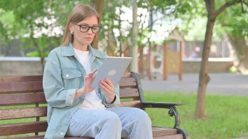 Young Woman Using a Digital Tablet on a Park Bench