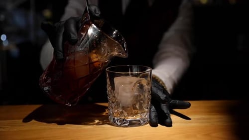 Bartender Pours Cocktail into Glass with Ice