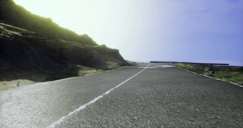Winding Coastal Road Under Bright Sky Near Rocky Cliff at Sunset