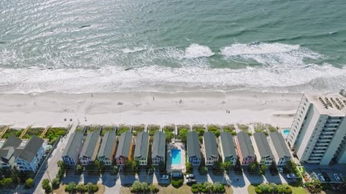 Drone establishing shot of colorful hotel houses and swimming pool in front of beautiful surfside be