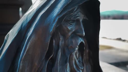 A smooth gimbal shot of a statue. A bearded and hooded old man looks on with gorgeous artistic deta