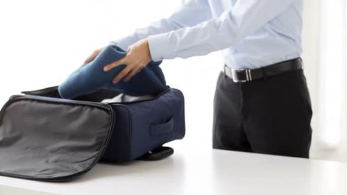 Man Packs Clothes into Blue Luggage Bag