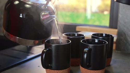 Pouring Hot Water into Black Mugs Indoors