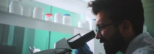 Man in Lab Coat Looking Through a Microscope