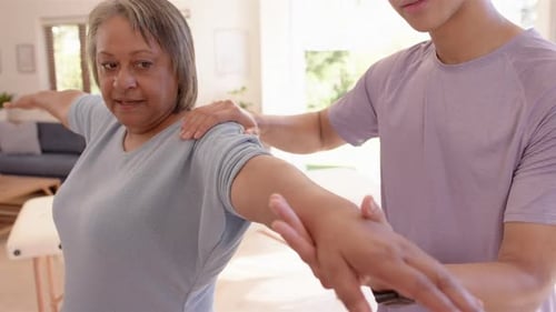 Physiotherapist assisting senior woman with arm stretching exercise in clinic