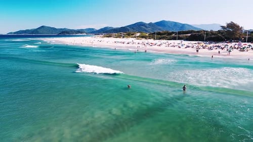 Aerial view of the sea with gentle waves and sandy beach with people relaxing on it