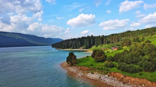 Lake with Clear Water and Stone Shore in Spruce Forest with Fir Trees Against a Daytime Sky