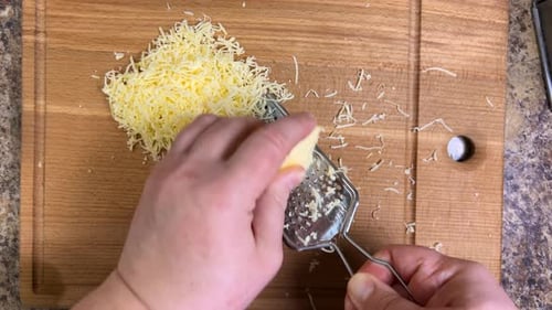 Hartkäse auf einer feinen Metallreibe gegen ein Holzbrett reiben. Ansicht von oben.