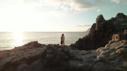 A couple embraces on the rocky coastline of Los Gigantes cliffs in Tenerife, Spain, with the sun set