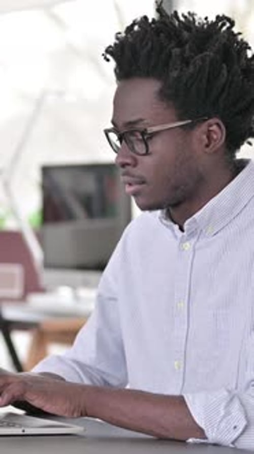 Young Adult Man Smiling and Typing on a Laptop