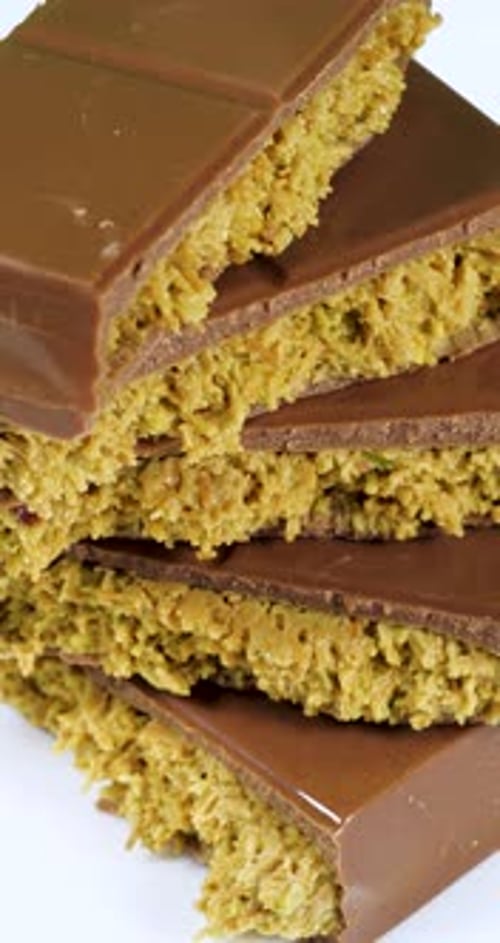 Barra de chocolate Trend Dubai con pasta de pistacho verde Kadayif y mantequilla de cacahuete que gira sobre blanco