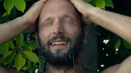 Handsome young man washing hair under shower in open bathroom garden super slow motion
