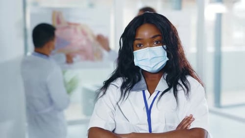 Young Woman Doctor in Mask with Arms Crossed