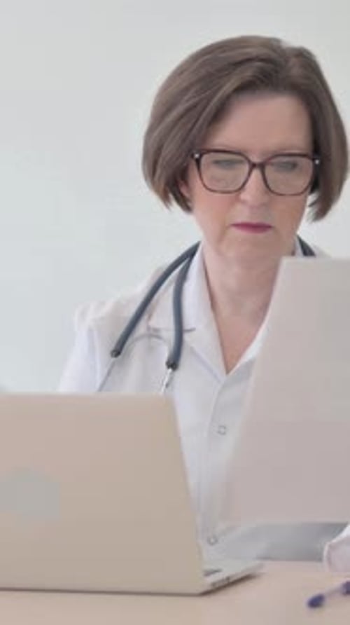 Médecin senior travaillant sur des documents et un ordinateur portable en clinique, Vidéo verticale
