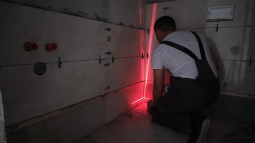 Man Tiling Bathroom Wall with Laser Level