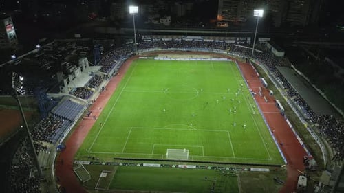 Drone Footage Capturing a Night Football Match in a Brightly Lit Stadium Spectators Fill the Stands