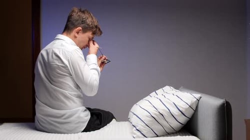 Man Sitting on Bed with Headache and Fatigue