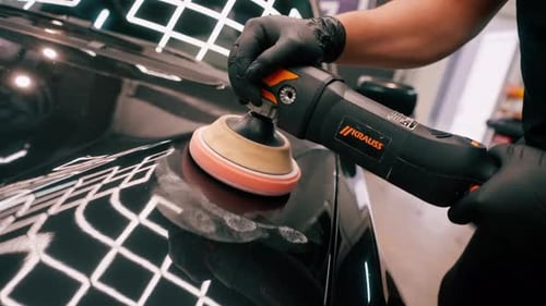 Close-up of a car wash worker using a polishing machine to polish the hood of black luxury car