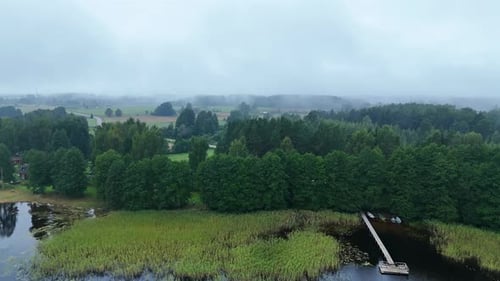 Drone flying from Lake pier toward misty countryside