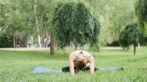 Man Stretching to Front and Warming Up Before Exercising on Yoga Mat Outdoors in a Park