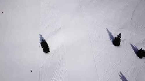 Skiers skiing downhill the ski slope during winter day in the high mountains, aerial view