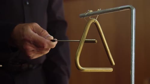 Close up percussion player hits triangle music instrument in orchestra