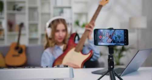 Chica adolescente bloguera que busca grabar una lección, tocando la guitarra. Mujer alegre tocando la guitarra