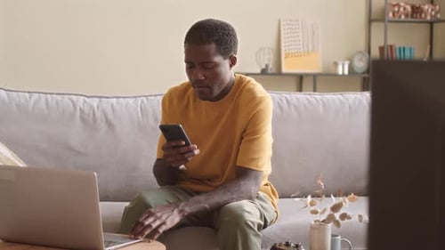 Man Using Phone and Laptop in Living Room