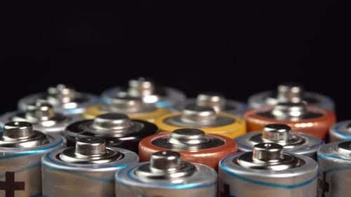 Rows of used alkaline AA batteries rotate on black background. Lithium ion battery pack close up