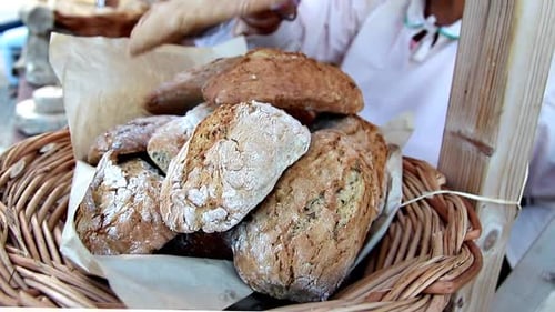 O padeiro medieval usa um conjunto de pinças para empilhar um pedaço de pão recém-assado em cima da cesta de pão A Ba